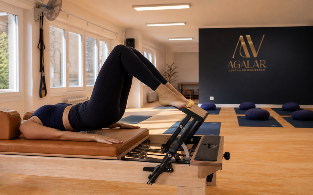 Mujer haciendo pilates reformer en la sala de Agalar Mungia con el logo AV de fondo