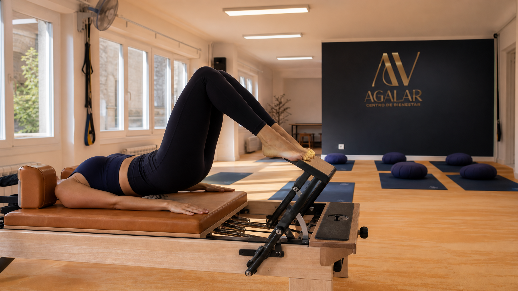 Mujer haciendo pilates reformer en la sala de Agalar Mungia con el logo AV de fondo